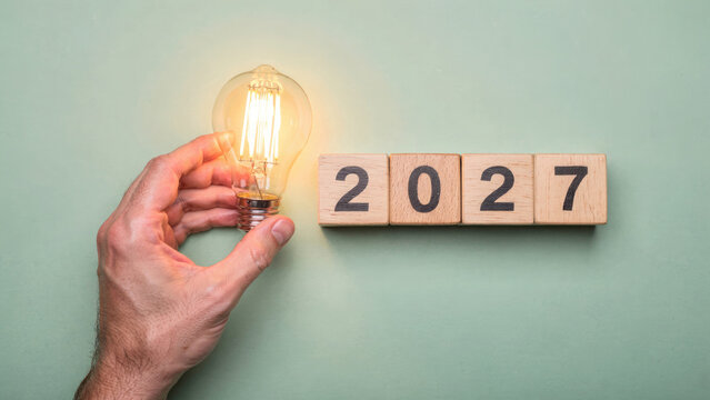 Hand holding lightbulb above wooden blocks spelling 2027 representing new year ideas
