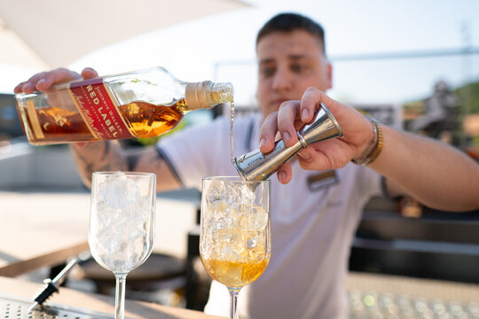LVIV, UKRAINE - JUNE 8, 2024: Bartender pouring Johnnie Walker Red Label whisky from a bottle into a metal jigger over a wine glass with ice
