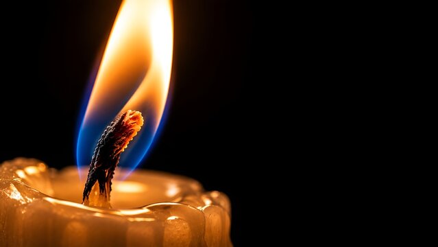 Extreme macro close up of a burning candle wick with glowing orange and blue flame on black background with copy space