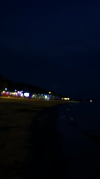 Blurry night seafront with distant colorful lights under deep blue sky and dark shoreline