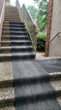 A textured rubber mat runner cascading down weathered concrete exterior steps creating a functional and geometric pathway through an urban stairwell