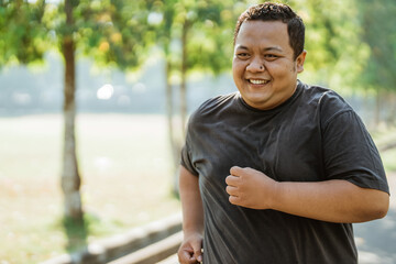 Fototapeta premium portrait of an overweight man with a smile while jogging in the morning at the park