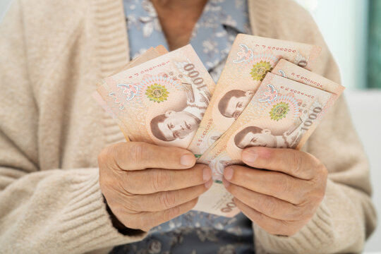 Asian elderly woman holding Thai banknotes money in hand. Poverty, saving problem in retirement.