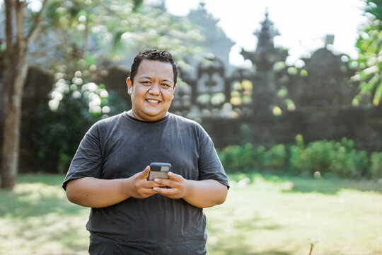 fat man smiles wearing handfree and holding cell phone after exercise in the park