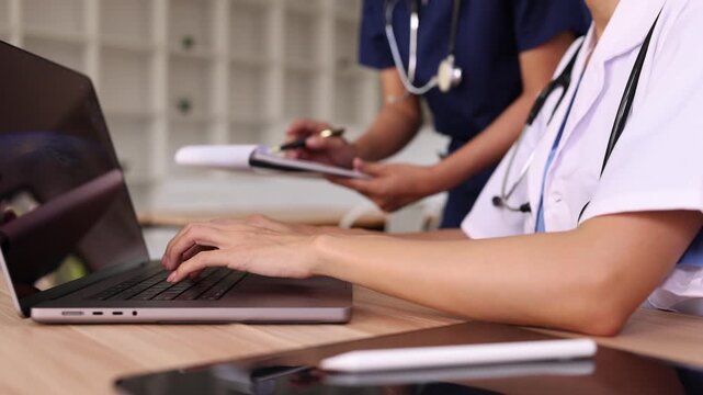 Asian female doctor and nurse discussing medical report on laptop in hospital.