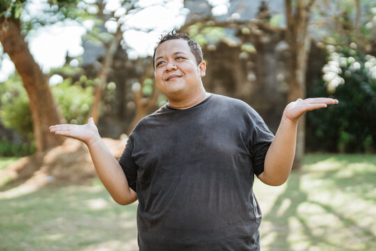 fat man standing with hand gestures offering something beside him in the outdoor background