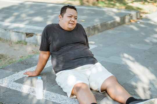 Asian fat man sits down to rest after jogging in the morning at the park
