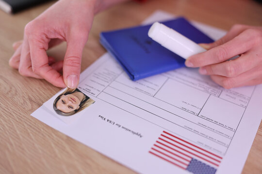 Applicant places portrait photo on United States visa form. Woman organizes passport and paperwork while preparing documents for immigration process