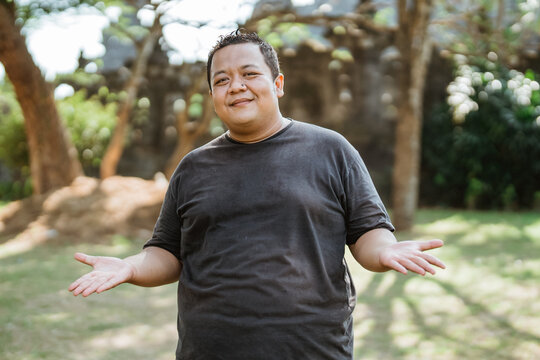 fat man wearing sportswear standing with hand gesture offering something in outdoor background