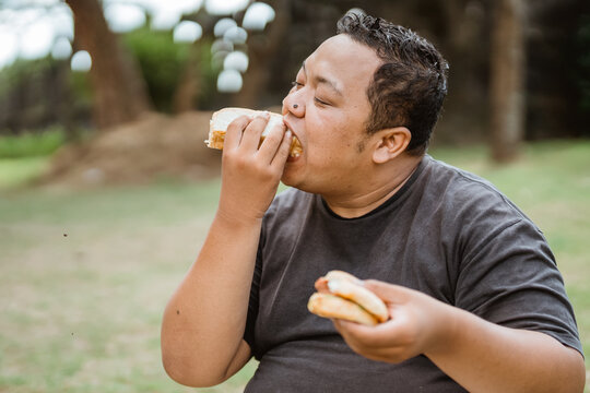 fat man eats hastily held bread while sitting in the park