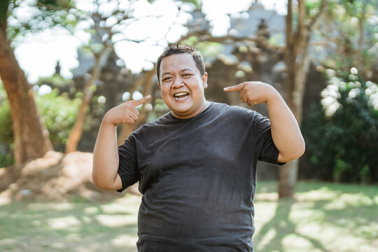 smiling Fat Man Standing with two hands pointing to his smile in outdoor background