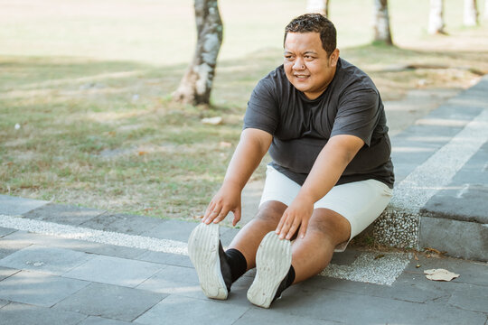 overweight man doing leg muscle stretching before exercise sitting in park