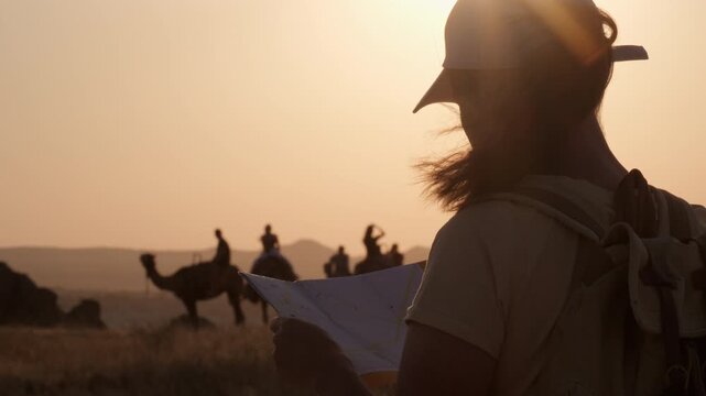 Woman traveler using paper map against desert landscape with camels at sunset