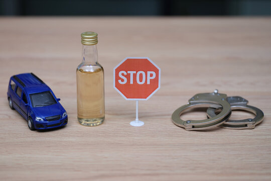 Miniature toy car at bottle of alcohol and pair of metallic handcuffs. Bright red Stop sign emphasizes serious message against drunk driving