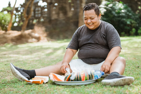 fat man sitting below with lots of sliced watermelon in front of him in the outdoor background