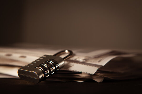 Padlock on pile of paper documents on dark background, closeup