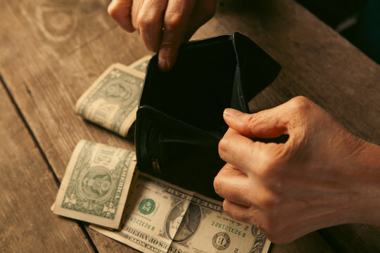 Elderly woman's hands open the wallet with money on a wooden table