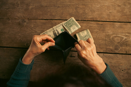 Elderly woman's hands open the wallet with money on a wooden table