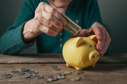 Elderly woman putting money into a piggy bank. Poverty concept
