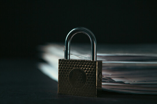 Padlock on pile of paper documents on dark background, closeup