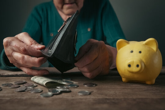 Elderly woman putting money into a piggy bank. Poverty concept