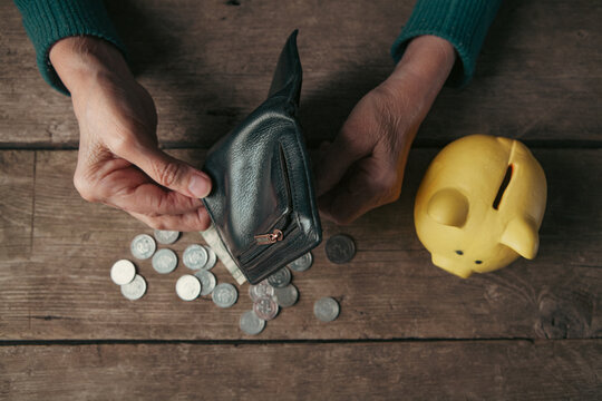 Elderly woman putting money into a piggy bank. Poverty concept