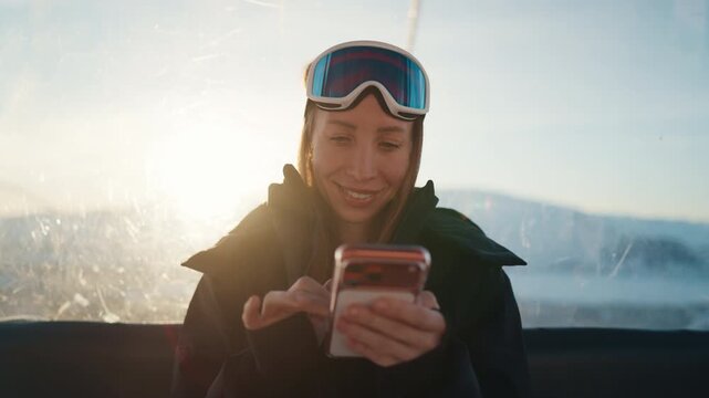 Female snowboarder and skier using smartphone in cable car in ski resort, phone addiction and mobile gadget overuse. Wide mobile net coverage area, roaming in traveling, enjoy moments and share posts
