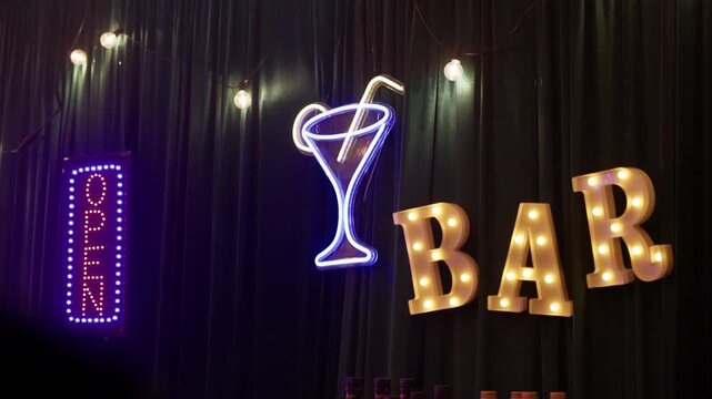 Neon open sign with martini glass and marquee bar letters glowing against dark curtain