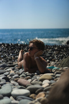 Woman in sunglasses relaxing on a pebble beach by the ocean