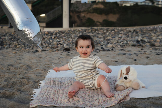 Joyful baby with a big silver balloon at the beach