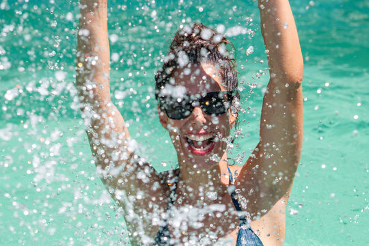 Happy woman splashing in a swimming pool on a sunny summer day