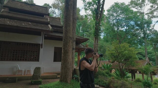 Male photographer taking photos at traditional temple in Chiang Mai, Travel photographer with mirrorless camera near historic Thai temple Wat Phra Lat surrounded by forest 4k