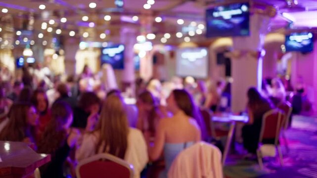 Blurred crowd inside lively banquet hall with colorful lights and seated guests at social gathering