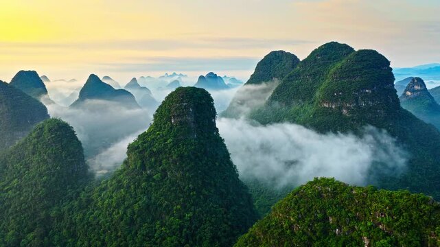 Drone aerial view of misty karst mountain peaks rising above low clouds at sunrise in Guilin, China