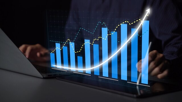 A businessperson analyzes digital financial data with virtual graphs on a laptop screen, focusing on market trends and growth projections in a modern workspace. Copula
