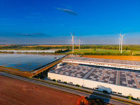 Industrial solar farm and rooftop panels. Solar energy installations cover rooftops and farmland adjacent to a asphalt highway.