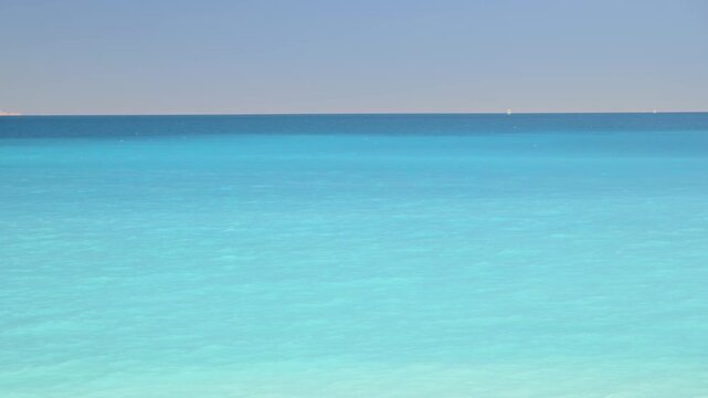 Beautiful turquoise ocean water gently rippling under a clear summer sky, creating a serene and minimalistic abstract background with different shades of blue and a distant horizon line