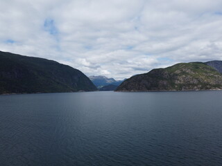 Majestic deep blue water flows between lush green mountains under a cloudy sky in a scenic Norwegian fjord during daylight hours. © nikjuzaili