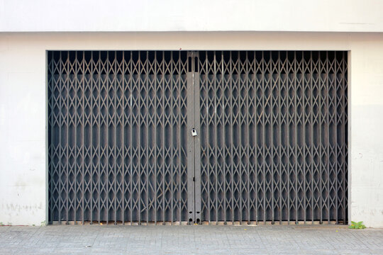 Folding metal gate with padlock, industrial steel scissor grille shutter door on closed store shop front, Ho Chi Minh City, Vietnam