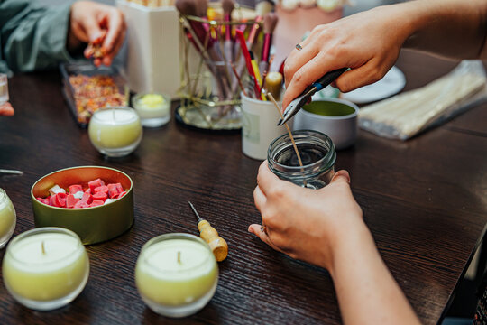 Participants work together at a candle making master class, using jars, wicks, wax pieces, tools, brushes, and decorative materials around a wooden table