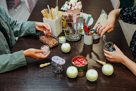 Participants work together at a candle making master class, using jars, wicks, wax pieces, tools, brushes, and decorative materials around a wooden table