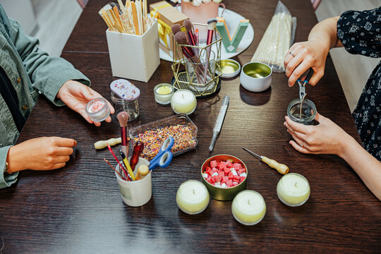 Participants work together at a candle making master class, using jars, wicks, wax pieces, tools, brushes, and decorative materials around a wooden table