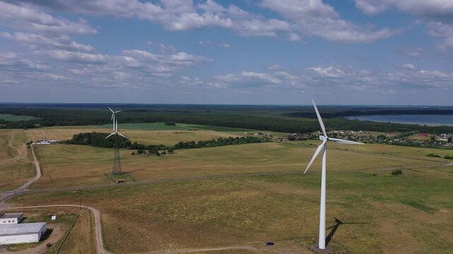 Majestic wind turbines stand tall against a backdrop of fluffy clouds and endless green fields.