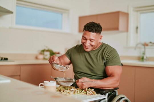Hispanic man in a wheelchair straining a warm banana peel infusion into a stoneware mug, showing capable self sufficiency in an accessible kitchen