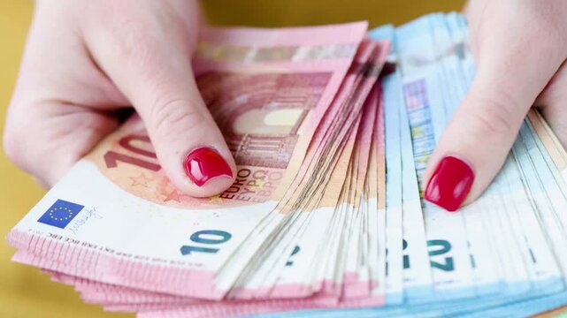 A pair of hands meticulously counts stacks of colorful euro banknotes at a cozy table. The vibrant hues catch the light, adding warmth to the inviting space.