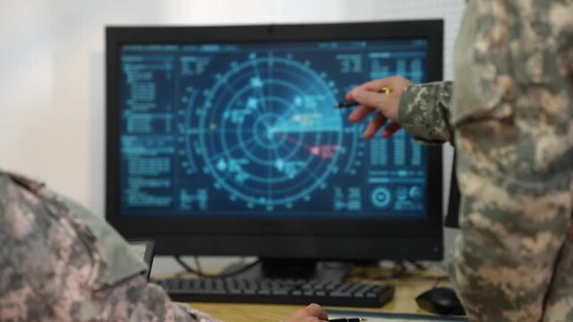 Soldier in camouflage points at a digital radar display on a computer monitor during a military command center briefing