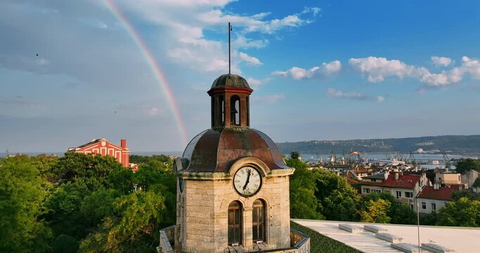  Historic clock tower of Varna city with bright rainbow in blue sky after rain in Bulgaria