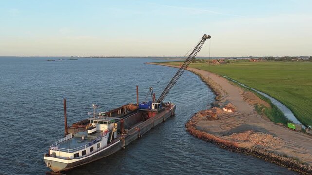 Aerial view of a dredging ship with a crane strengthening a coastal dike. Construction works for flood protection and land reclamation