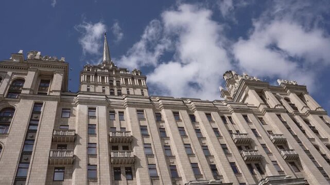 Low-angle view of ornate historic high-rise facade with spire under partly cloudy blue sky, with building, architecture, facade, masonry detail, showing stone, limestone, column, pilaster context