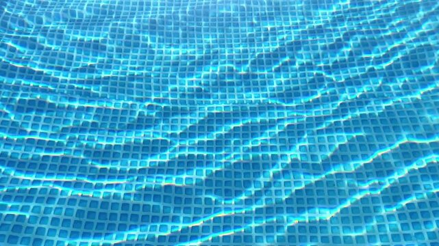 High-angle shot of clear, rippling blue water reflecting sunlight over a tiled swimming pool bottom. Ideal for summer travel promos, pool maintenance ads, and resort media.